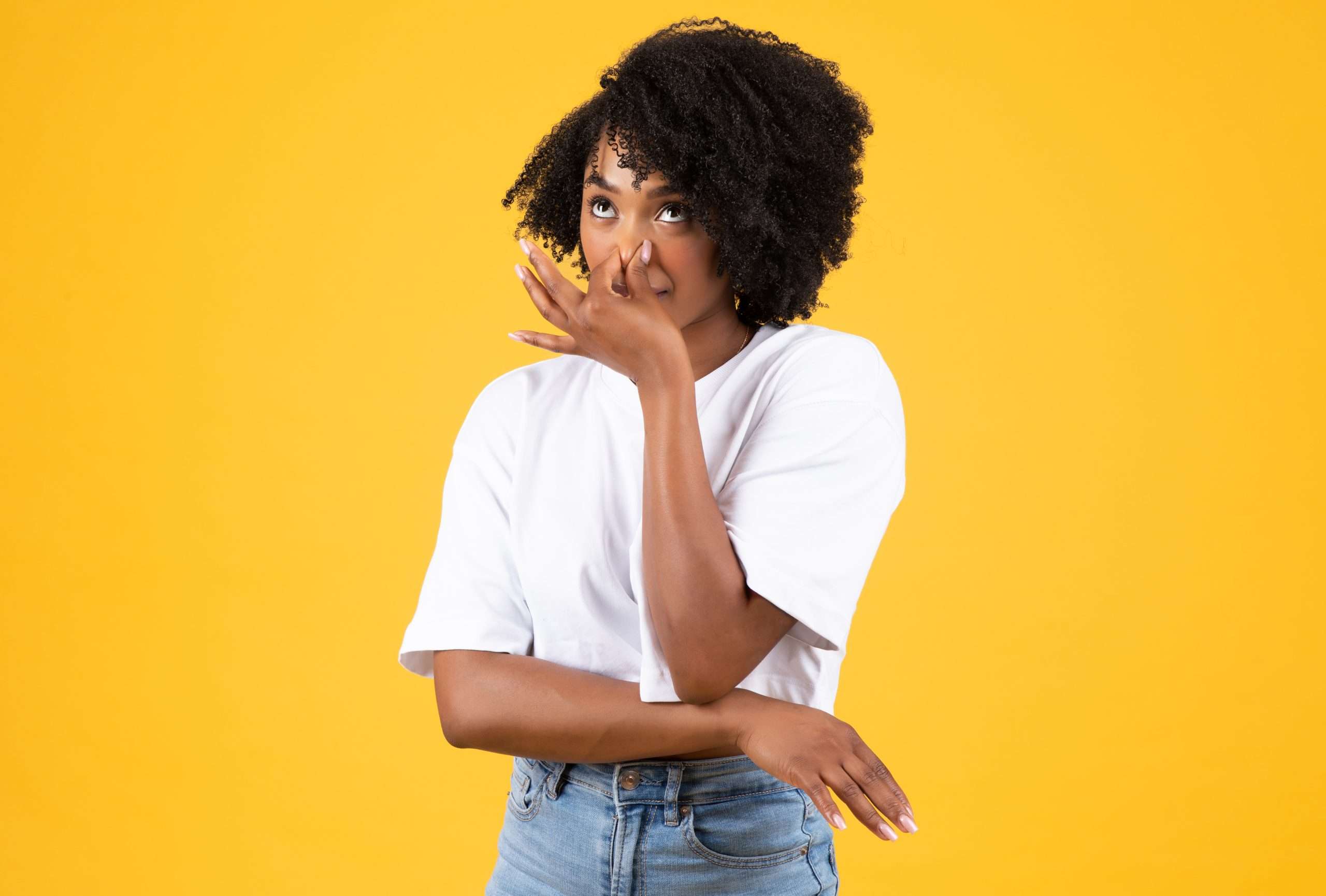 Dissatisfied millennial african american curly woman in white t-shirt covering nose with hand