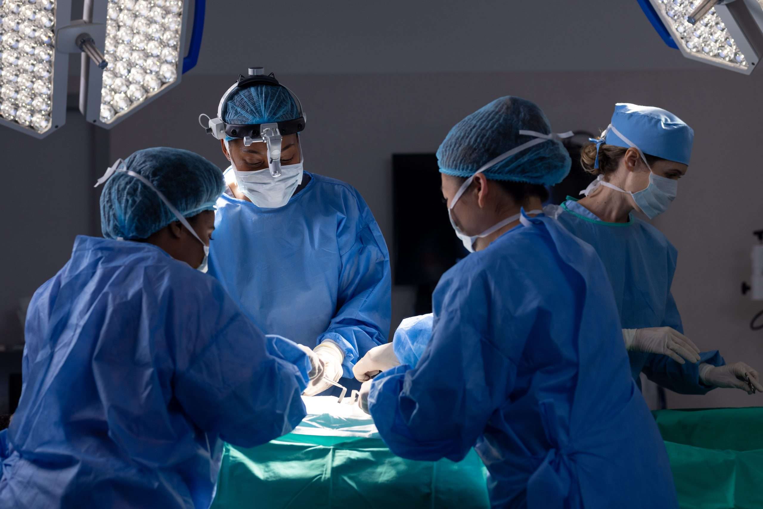 Diverse female doctors with face masks doing surgery in hospital operating room. Medicine, healthcare and medical services, unaltered.