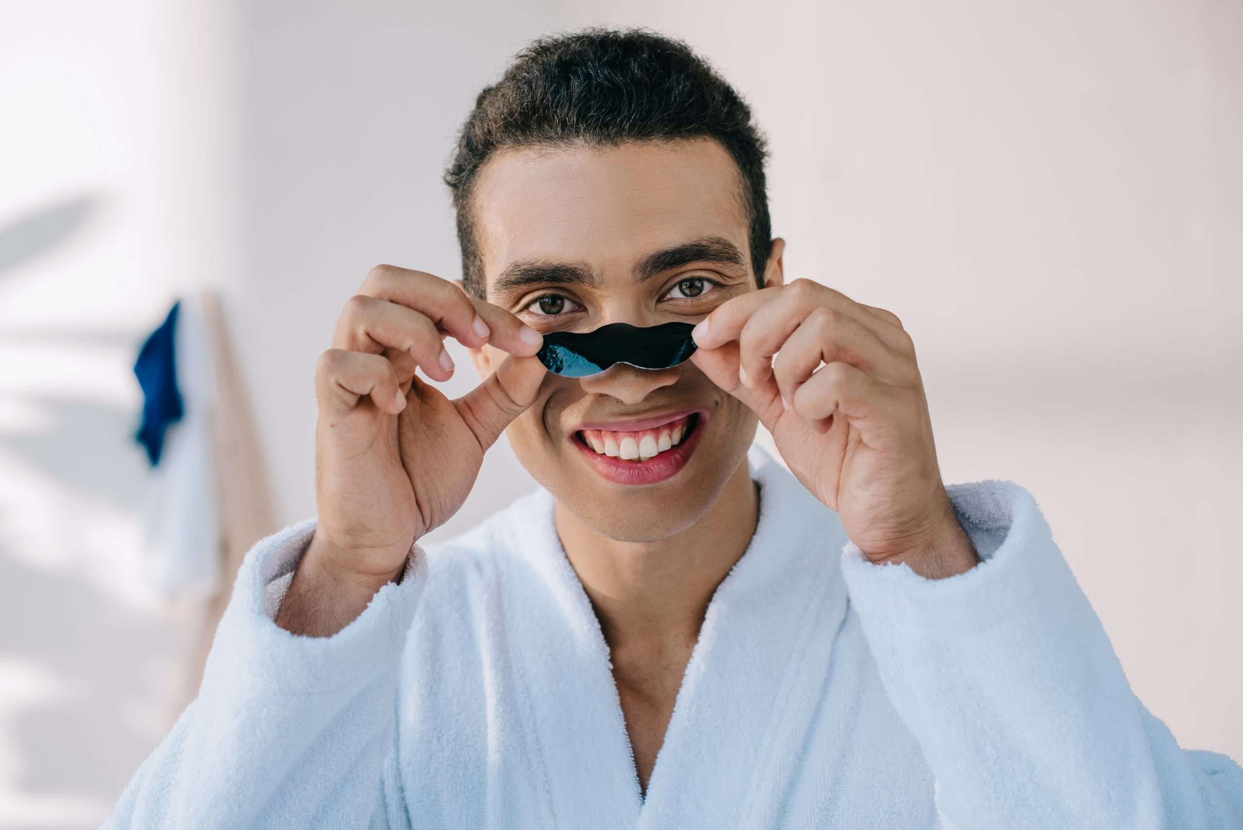handsome young man putting nose strip on face while looking at camera