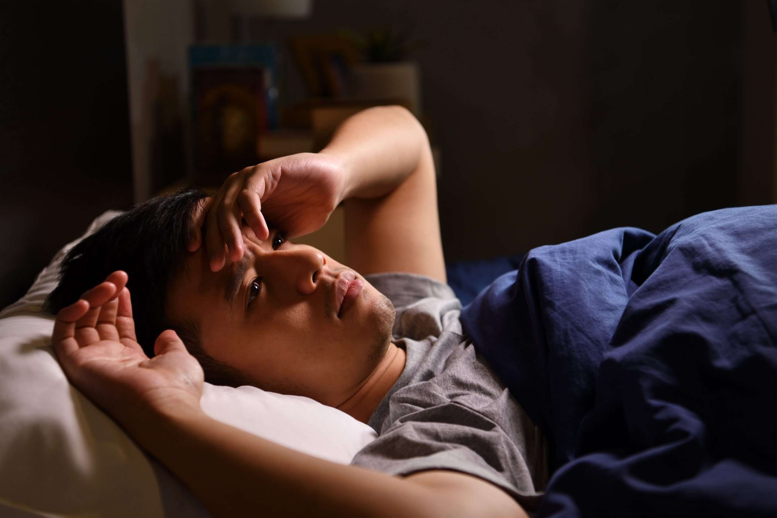 A depressed young man suffering from insomnia lying in bed